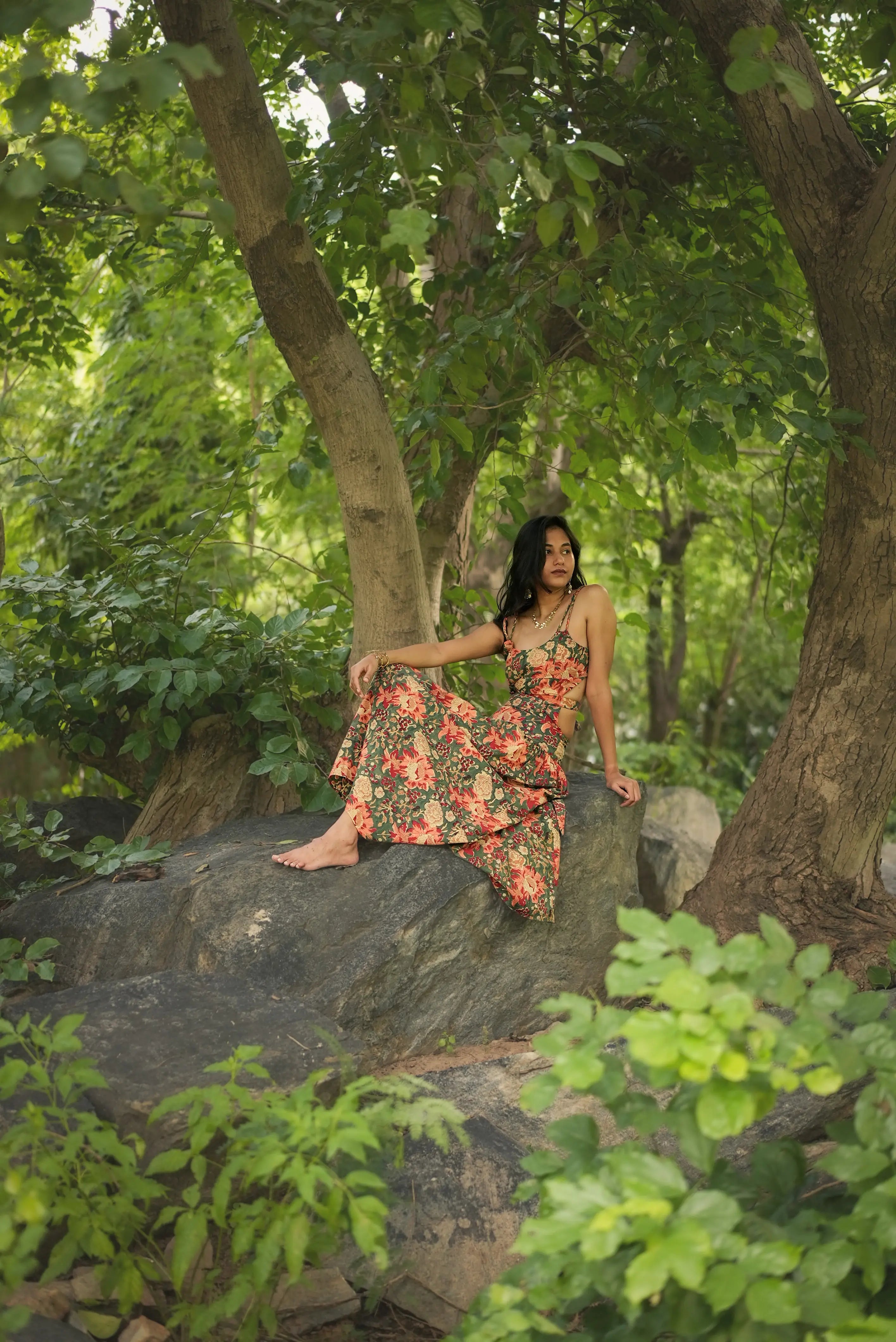 Woman in a floral dress sitting on a rock in a forest