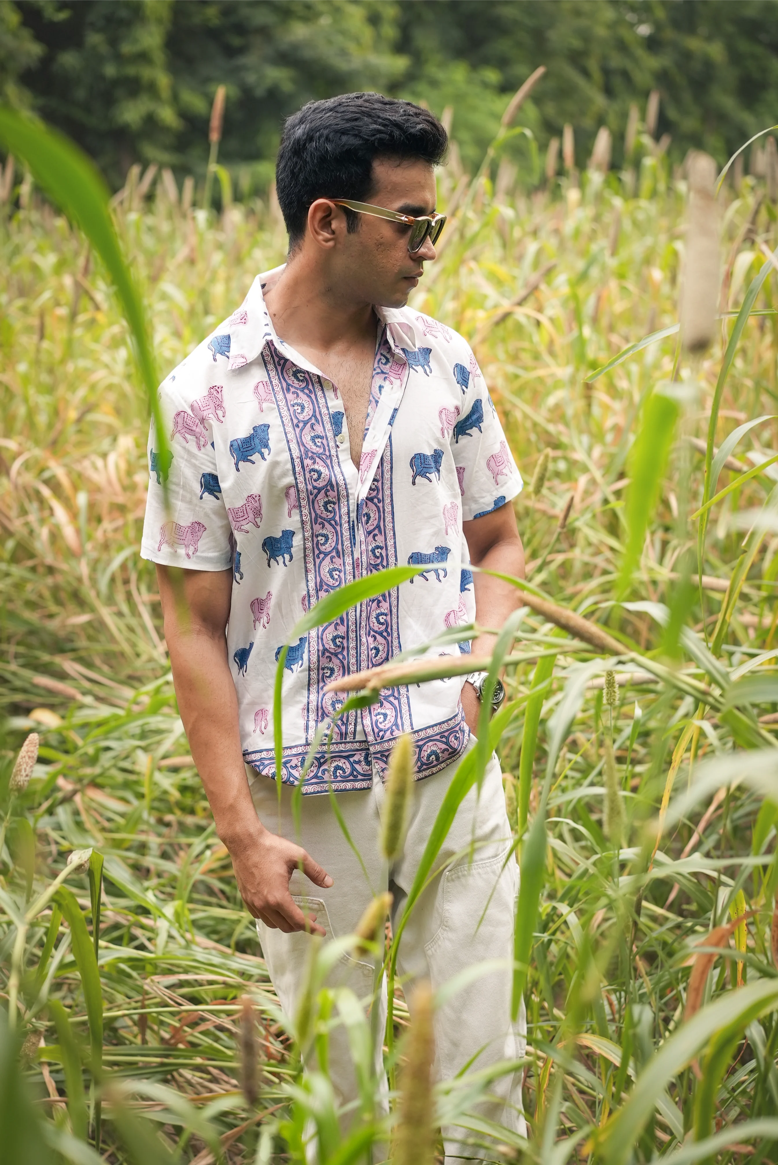 Man wearing a patterned Sattva and Sage shirt and sunglasses, standing in a field of tall grass.