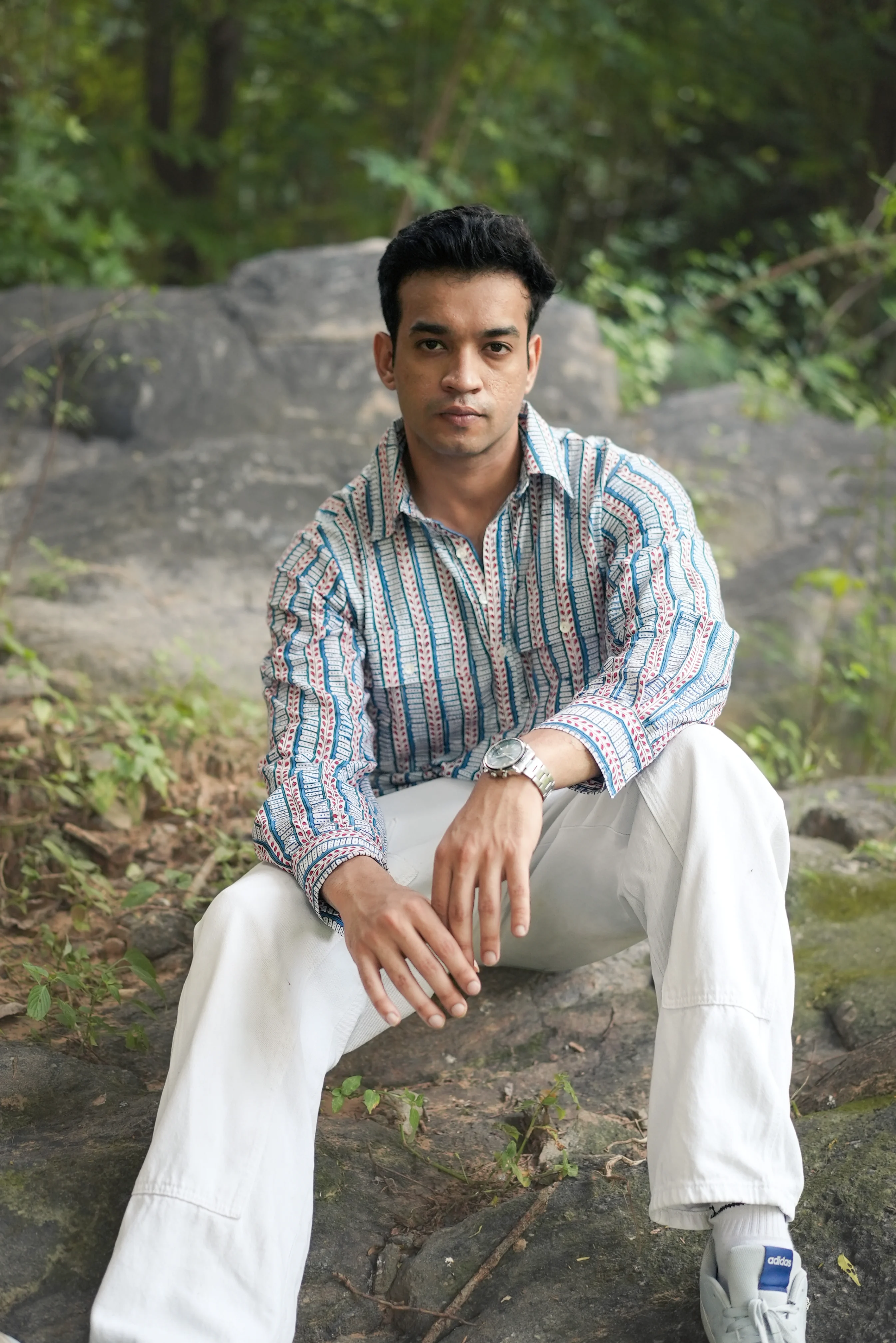 Man wearing Sattva and Sage clothing, sitting on a rock with a natural background.