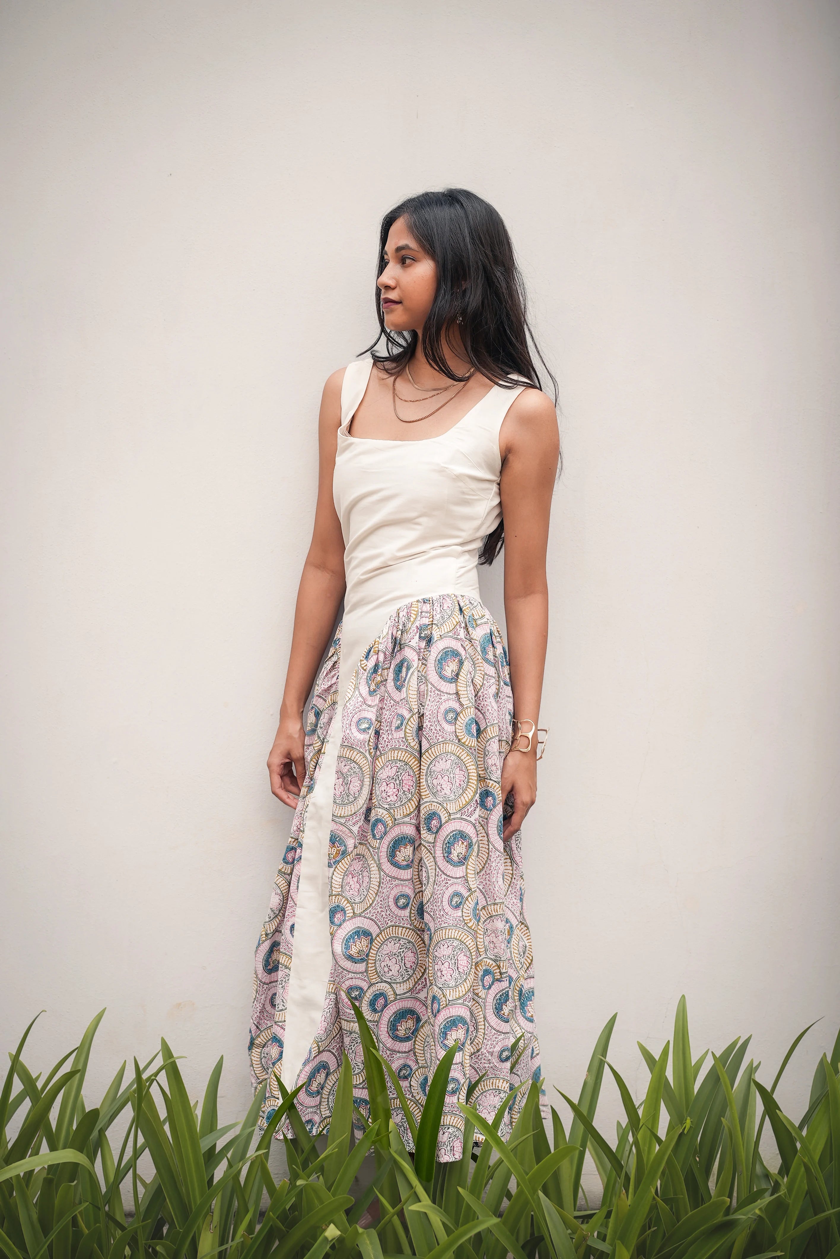 Woman in a white top and patterned skirt standing in grass with a plain background