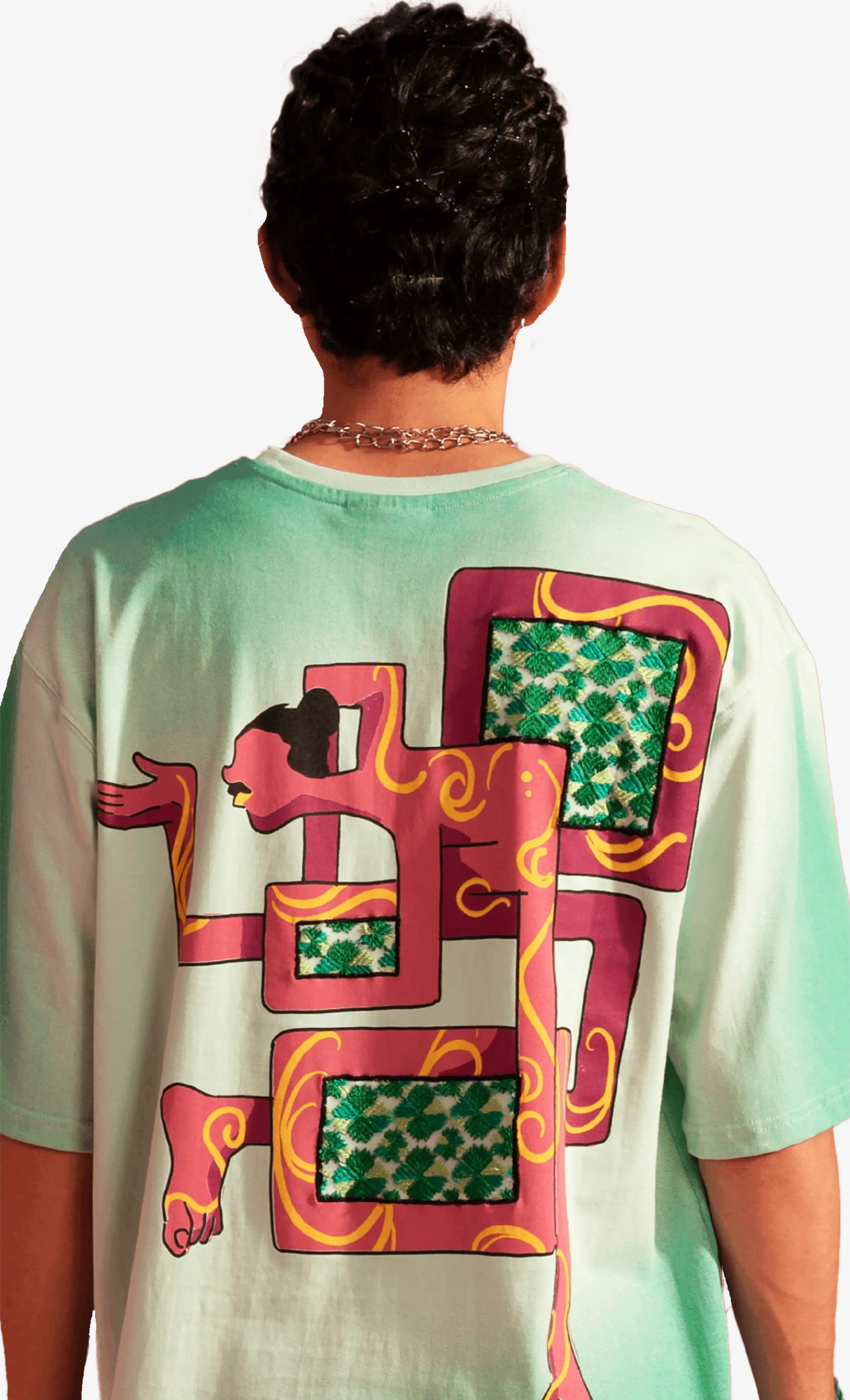 Person wearing a light green Sattva and Sage t-shirt with a colorful graphic design on the back.