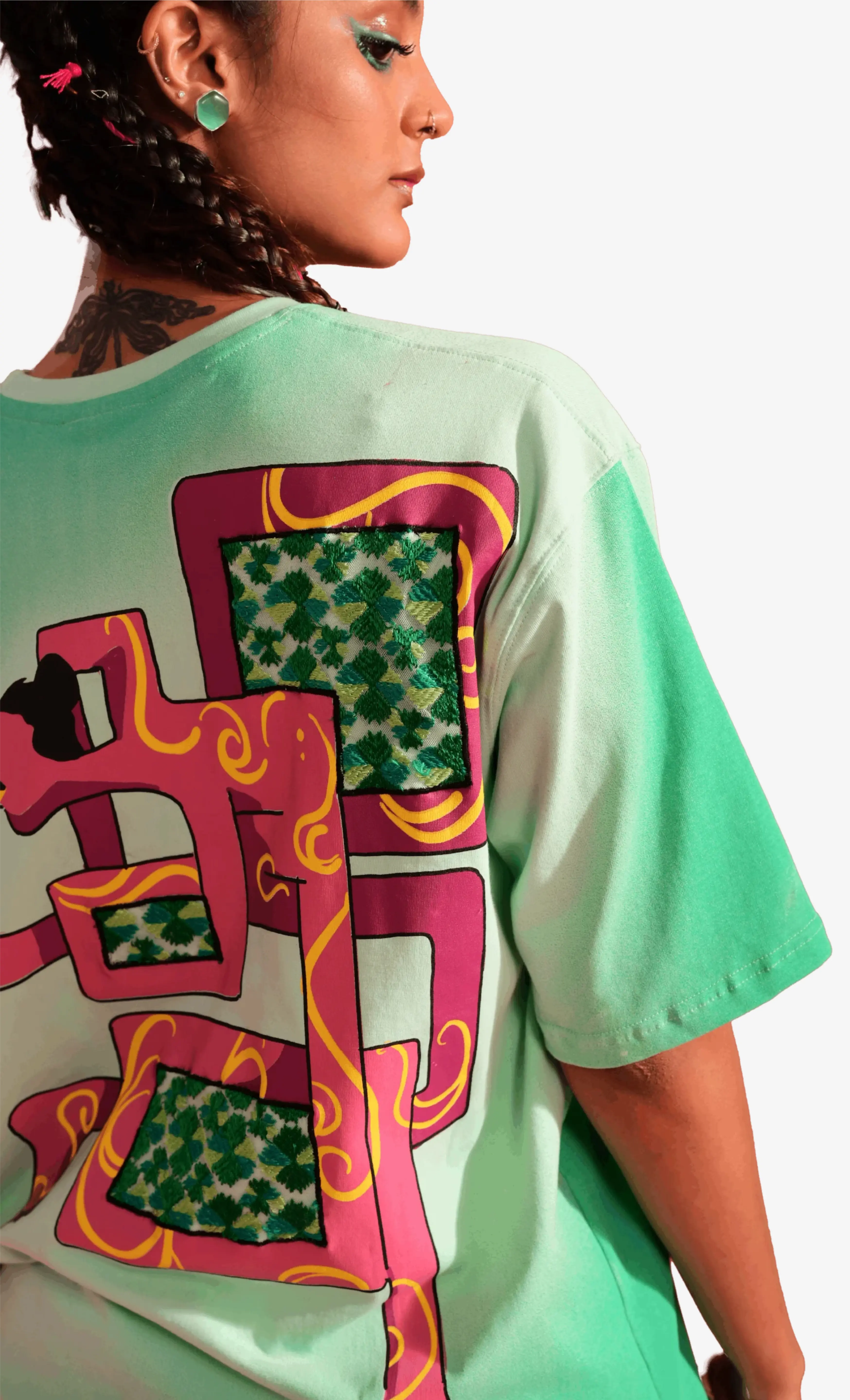 Person wearing a green Sattva and Sage t-shirt with a colorful graphic design on a plain background.