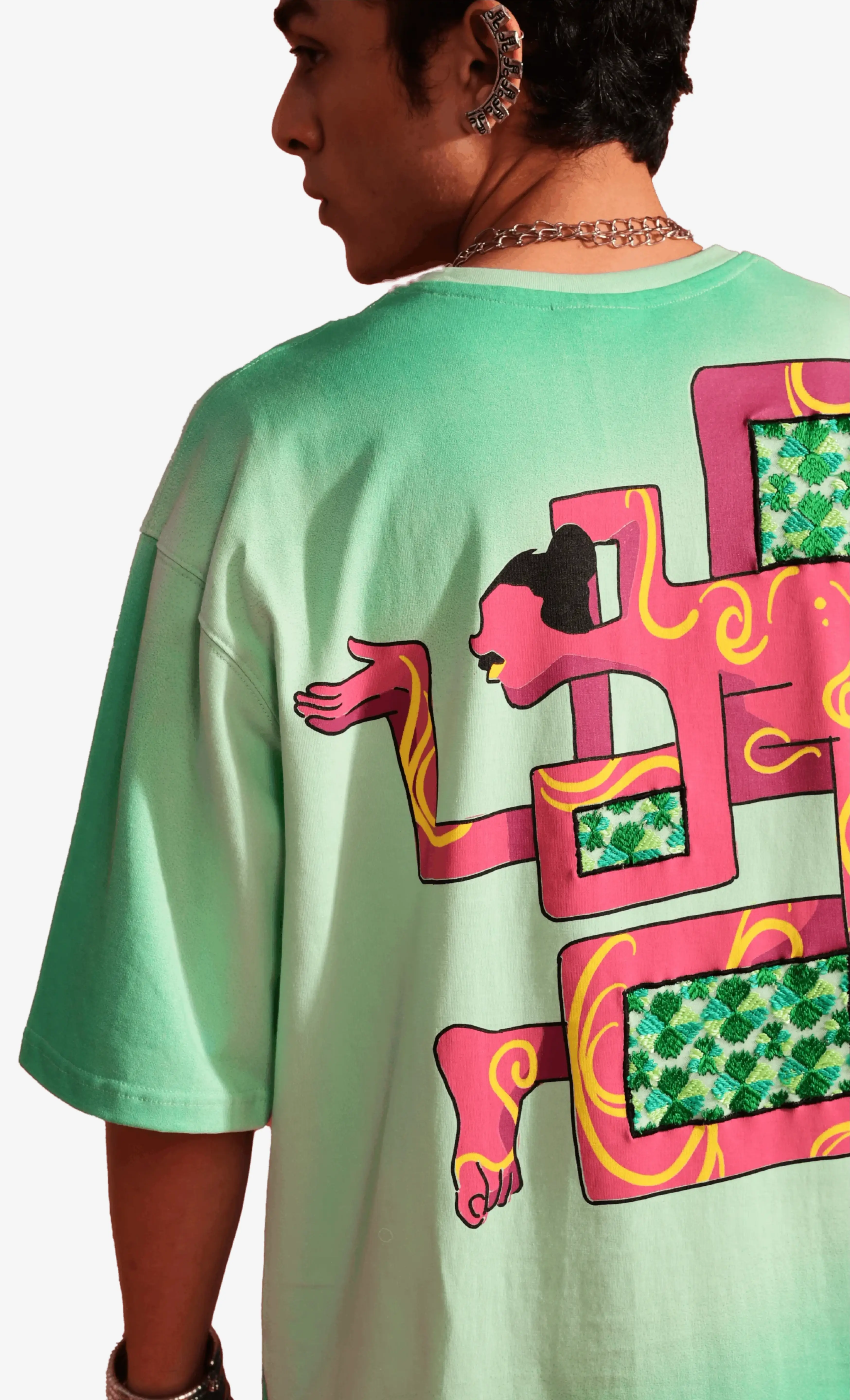 Person wearing a light green Sattva and Sage t-shirt with a colorful graphic design on the back.