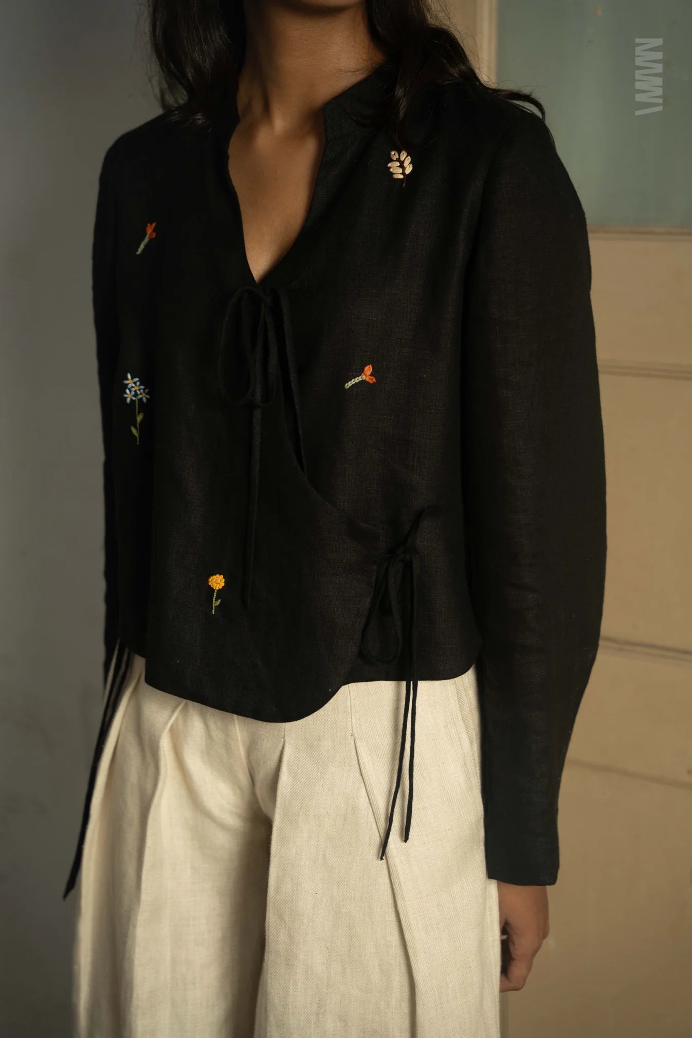Person wearing a black embroidered blouse with beige pants against a neutral background