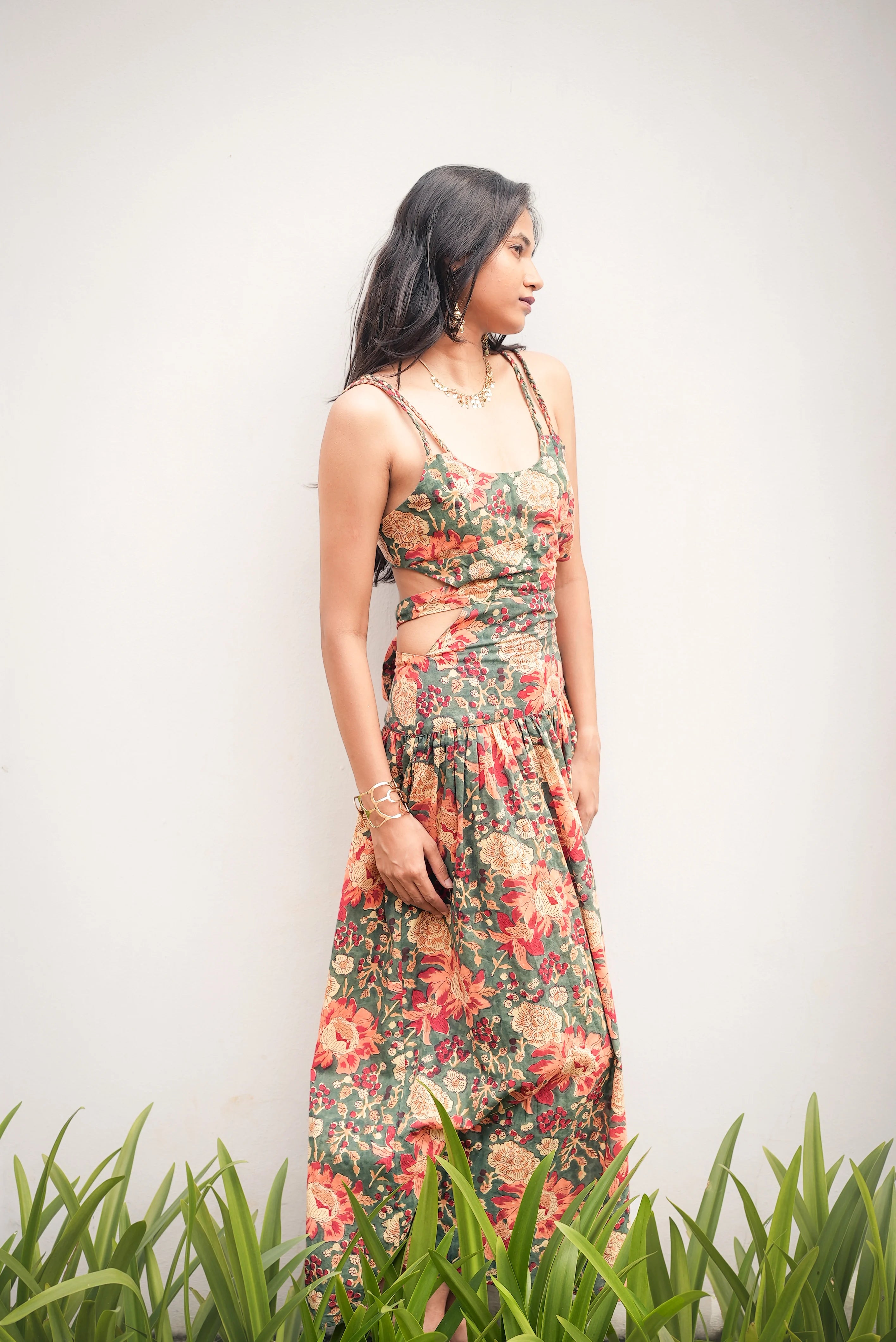 Woman wearing a floral dress standing in front of a white wall with green grass at the bottom.