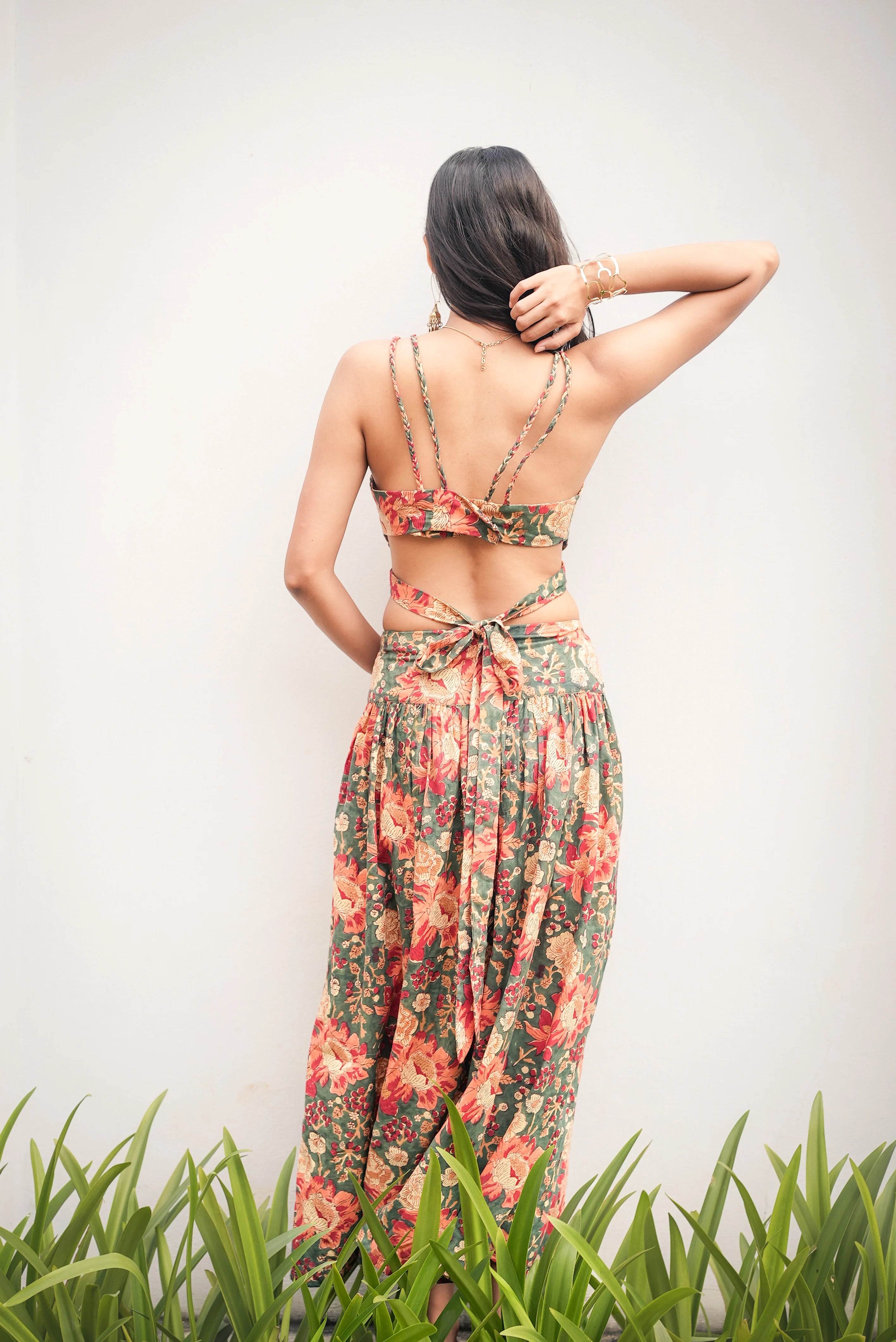 Woman wearing a floral dress standing in front of a white wall with green grass at the bottom.