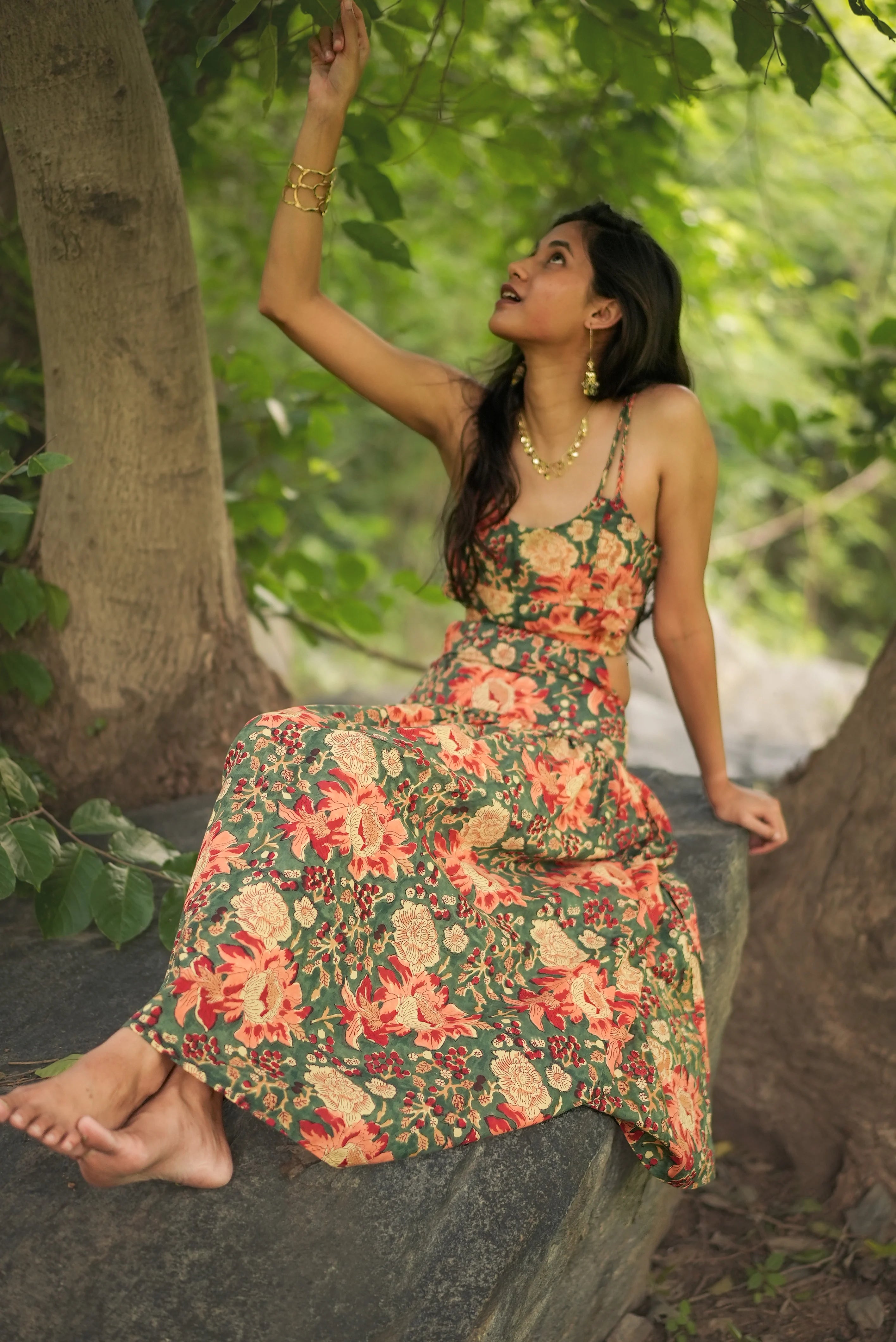 Woman in a floral dress sitting on a rock with greenery around