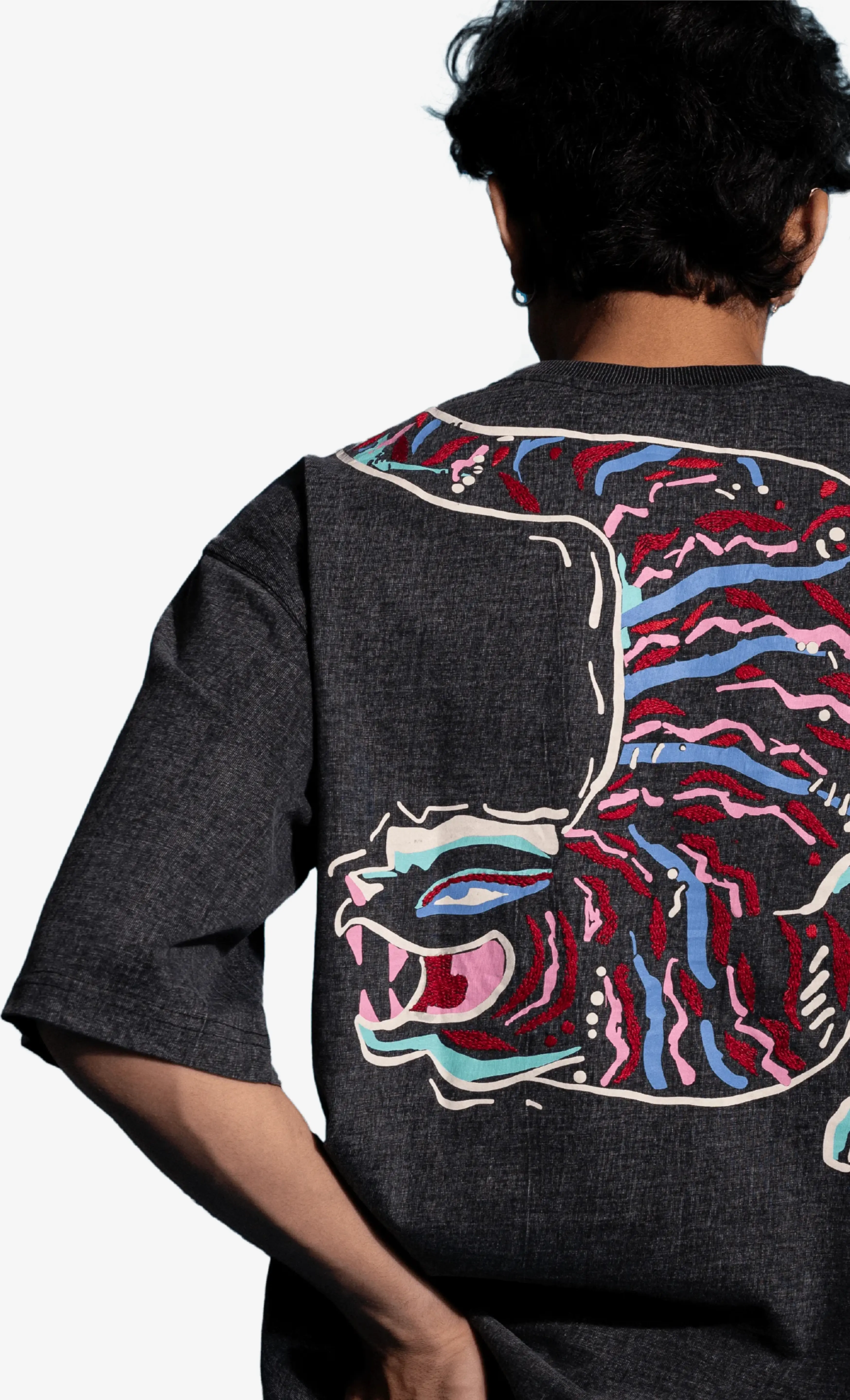 Person wearing a black Sattva and Sage t-shirt with a colorful tiger design on the back against a white background.