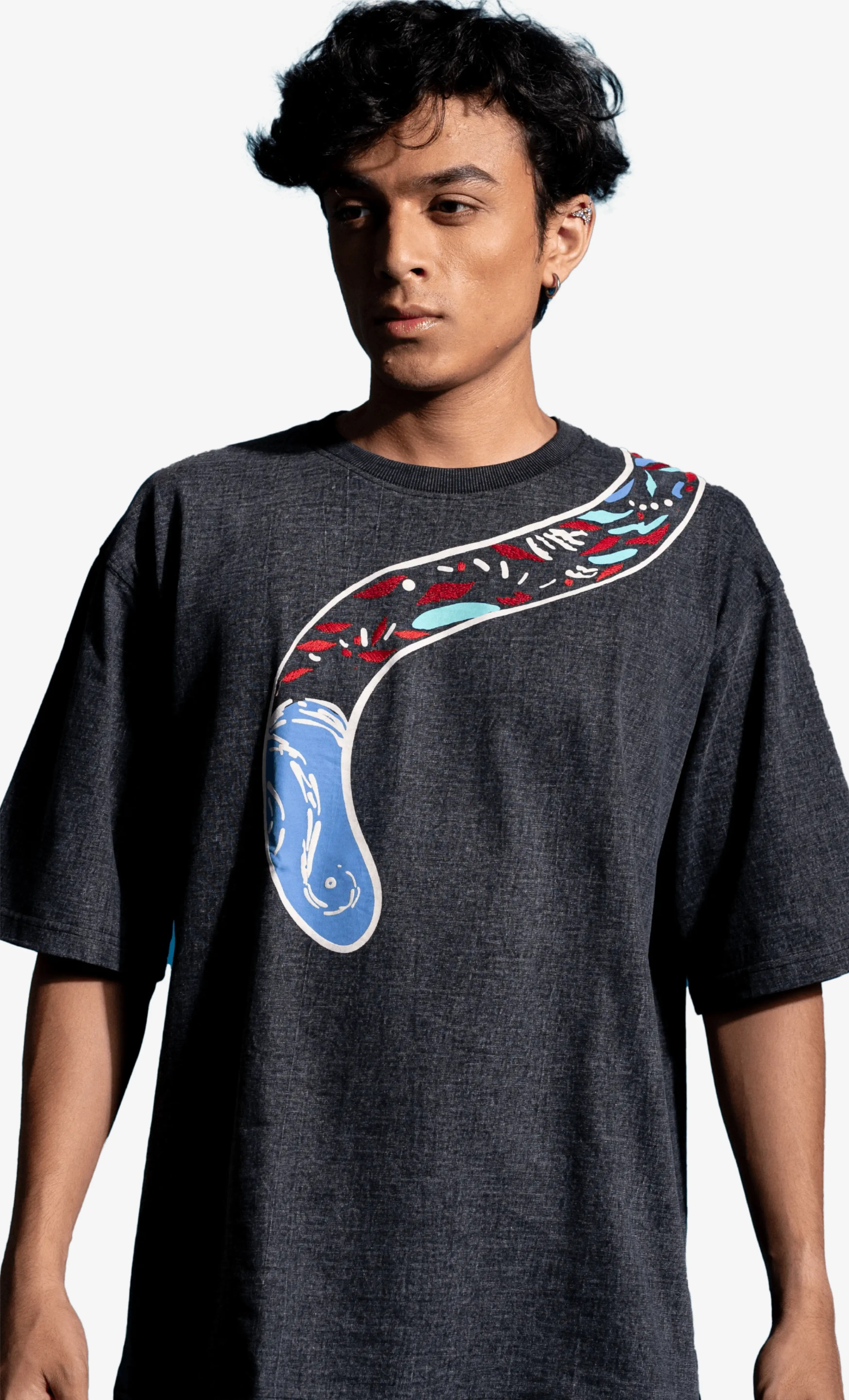 Person wearing a dark gray Sattva and Sage t-shirt with a colorful graphic design on a white background.